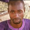Portrait of a man wearing a purple shirt with a stone wall background.